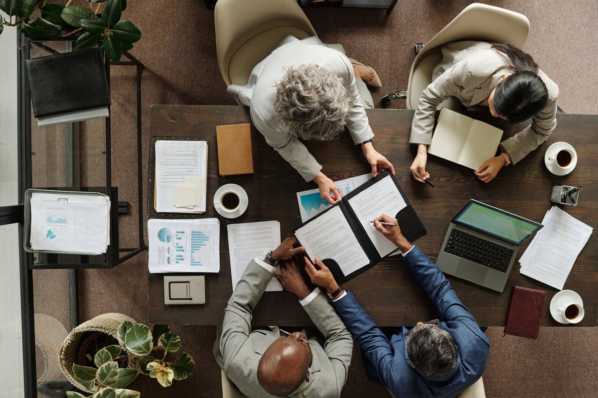Real estate investors reviewing contracts and deal numbers around a table with a laptop